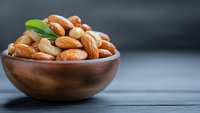 Mixed nuts and almonds in wooden bowl on rustic table surface for healthy snacking and cooking ingredients.