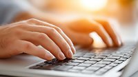 Close-up of hands typing on laptop keyboard in warm sunlight for business productivity and remote work concepts.