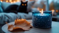Cozy autumn evening with blue scented candle in decorative glass holder, dried maple leaf, and black cat silhouette against blurred bokeh lights background.