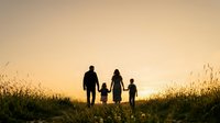 Silhouette of family with two children walking through golden wheat field at sunset, holding hands together during outdoor leisure activity.