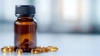 Amber glass bottle with omega-3 fish oil capsules scattered on white surface against blurred background. Nutritional supplement and vitamin concept.