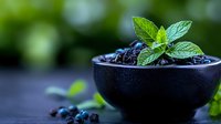 Fresh ripe blueberries in black ceramic bowl with mint leaves on dark background, selective focus. Natural organic berries for healthy eating.