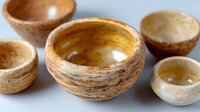 Rustic ceramic bowls with textured surface and natural earth tones arranged on light background. Handcrafted pottery showcases organic shapes and weathered finish.