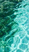 Crystal clear turquoise water surface with rippling waves and light reflections creating abstract patterns for summer vacation and tropical themes.