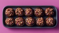 Chocolate muffins with nuts in black baking pan on pink background. Homemade bakery treats for breakfast or dessert preparation in kitchen.