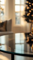 Blurred festive interior with glass table reflection and golden bokeh lights from Christmas tree, creating warm atmospheric holiday ambiance in modern living room.