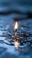 Burning match standing in water with glowing flame reflection, dramatic dark blue background with ripples and droplets creating surreal atmospheric scene.