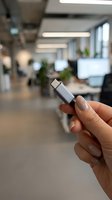 Close-up of female hand holding USB-C connector cable in modern office environment with blurred workspace background, suitable for tech and business applications.