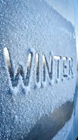 Word winter carved in frost-covered surface with ice crystals, cold blue tones evoking freezing season atmosphere for seasonal design.