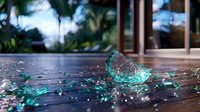 Shattered turquoise glass fragments scattered on wooden floor with natural light and bokeh effect creating dramatic atmosphere for conceptual design.