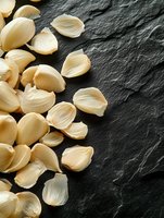 Fresh peeled garlic cloves scattered on dark slate stone background with copy space, macro food photography for cooking and culinary concepts.
