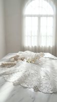 Elegant white wedding dress with intricate lace details and pearl accessories laid on bed near arched window in bright bridal preparation room.