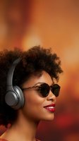 Young African American woman with curly afro hair wearing sunglasses and headphones smiling against warm orange gradient background for music and lifestyle content.
