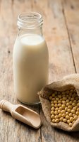 Fresh soy milk in glass bottle with soybeans in burlap sack on rustic wooden table for healthy plant-based nutrition and dairy alternative beverages.