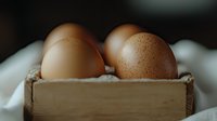 Fresh brown chicken eggs in rustic wooden box on white textile background with soft natural lighting and shallow depth of field.