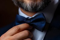 Mature businessman adjusting elegant navy blue polka dot bow tie with hand, formal menswear and professional attire for special occasions and events.