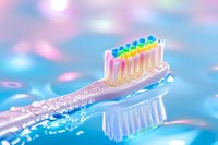 Clear plastic toothbrush with rainbow colored bristles on blue background with pink bokeh lights, dental hygiene concept for oral care and healthy lifestyle.