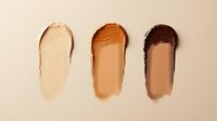 Foundation makeup swatches in light, medium and dark skin tones smeared on beige background showing texture and coverage for cosmetic product photography.