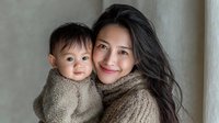 Asian mother and baby boy in matching brown knit sweaters sharing tender moment together indoors with soft natural lighting for family lifestyle content.