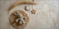 Cozy nursery composition with handmade crochet bunny toy on round fur rug, hanging wooden star and moon decorations, and wheat stalk in neutral beige tones.