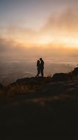 Romantic couple silhouette embracing on mountain peak during golden hour sunset with dramatic sky and valley view below for love and adventure concepts.