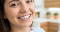 Young Hispanic woman with metal braces smiling confidently in modern kitchen, showing dental orthodontic treatment progress for healthy teeth alignment.