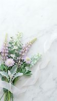Soft pastel wildflower bouquet with lavender lupins and eucalyptus tied with sheer ribbon on white marble background.