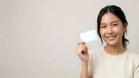 Young Southeast Asian woman with dark hair wearing a cream-colored shirt, smiling while holding a blank white card against a neutral background for business, marketing, or promotional use.