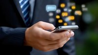 Business professional in dark suit using smartphone with floating social media and messaging icons, depicting modern digital communication and networking.