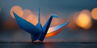 Blue origami crane with orange interior against blurred bokeh background at sunset, symbolizing peace and tranquility.
