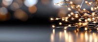 Glowing warm LED string lights creating magical bokeh effect on reflective surface against dark background, festive holiday atmosphere and decorative lighting.