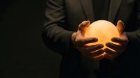 Businessman in suit holding glowing orb of light in cupped hands against dark background. Concept for innovation, ideas, energy, and business solutions.