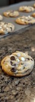 Fresh baked chocolate chip cookies with white chocolate chips on granite countertop, soft and chewy texture visible, shallow depth of field focus on single cookie.