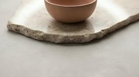 Terracotta ceramic bowl sitting on rustic stone coaster against neutral background, suitable for home decor, product photography, and lifestyle styling.