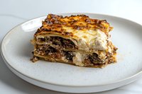 Traditional layered lasagna with ground beef, melted cheese and bechamel sauce served on round white ceramic plate, close up view of single portion.