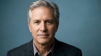 Middle-aged man with gray hair and light skin tone wearing a dark blazer over a light shirt, professional headshot against blue background for corporate, business, and executive use.
