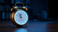 Vintage brass alarm clock showing nearly midnight on wooden desk in dimly lit room with blue ambient lighting for time management concepts.