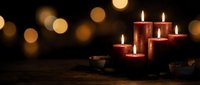 Red candles burning with warm flames on wooden surface against dark background with golden bokeh lights creating cozy atmospheric mood for relaxation.