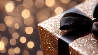 Elegant gift box wrapped in sparkling gold paper with black satin ribbon against blurred bokeh lights background for holiday celebration.