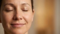 Peaceful middle-aged Caucasian woman with closed eyes and serene expression showing natural skin texture and gentle smile in warm indoor lighting.