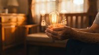 Hands gently holding glowing vintage Edison bulb in warm cozy interior setting symbolizing creativity innovation and bright ideas for business concepts.