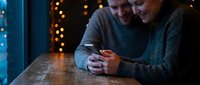 Happy couple embracing at wooden table with warm bokeh lights creating romantic atmosphere for Valentine's Day celebration and intimate moments together.