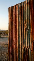 Weathered corrugated metal fence with heavy rust and oxidation in desert landscape at sunset, showing aged industrial texture and decay for background and design use.