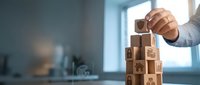 Hand stacking wooden blocks with insurance and finance icons, symbolizing protection, security, and risk management in business planning.