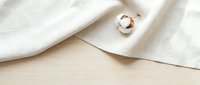 Elegant rose gold wedding ring with geometric design on soft white fabric against natural wood surface for jewelry photography and branding materials.