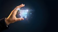 Hand holding glowing shopping cart icon with sparkling effects on dark background for e-commerce and online retail business concepts.