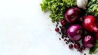 Fresh red onions, garlic, and green lettuce leaves arranged on white background with scattered black pepper and cranberries creating culinary composition.