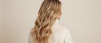 Young blonde woman with long wavy hair wearing cream sweater against neutral background for fashion and lifestyle content.
