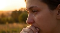 Young woman crying with tears on face during golden hour sunset showing emotional distress and sadness in natural outdoor setting.