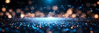 Magical glowing blue and gold particles scattered on reflective surface against dark background with bokeh lights creating dreamy atmosphere.